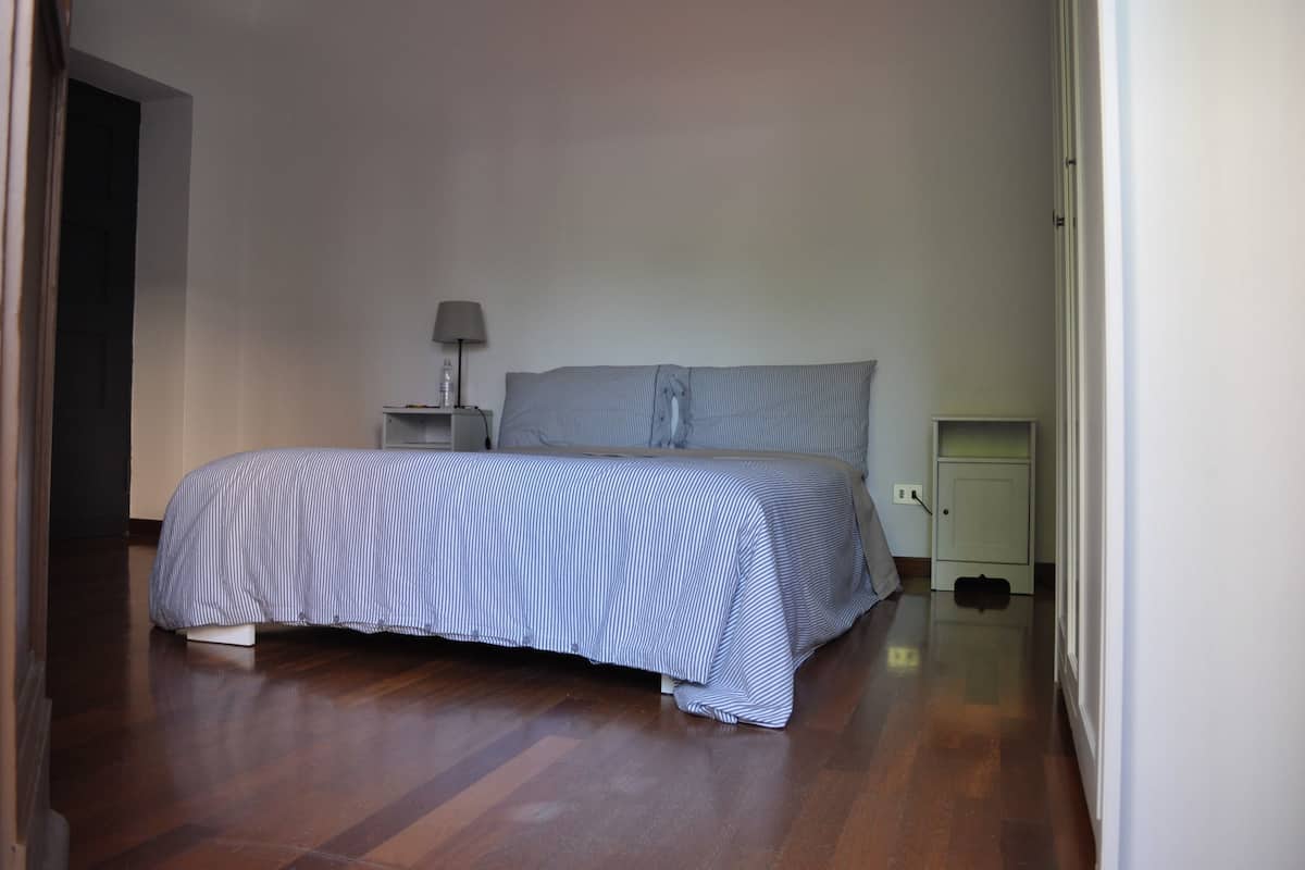 A bedroom with a bed, a nightstand with a lamp, and a small cabinet.