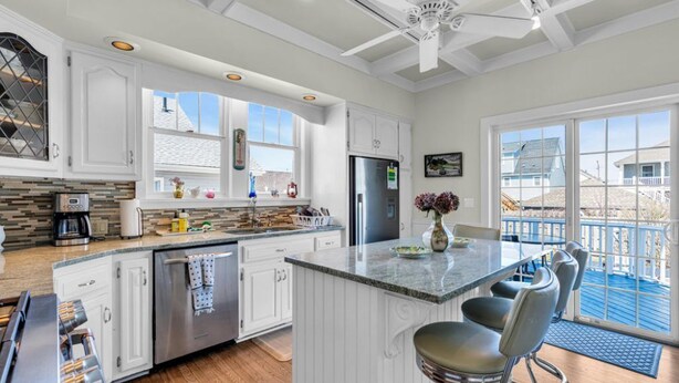 A modern kitchen with white cabinetry, a central island with bar stools, a stainless steel refrigerator, and a large window offering a view of the outside.