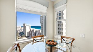 A dining area with a view of the city and ocean, a round glass table, and two wooden chairs. - Beach Colony West 15A- 3BD/3BA Gulf front w/Beach Service & Onsite Management (Navarre Beach)