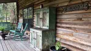 Una cabaña de madera con un letrero que dice 'WELCOME', sillas verdes y una planta en maceta en el porche.