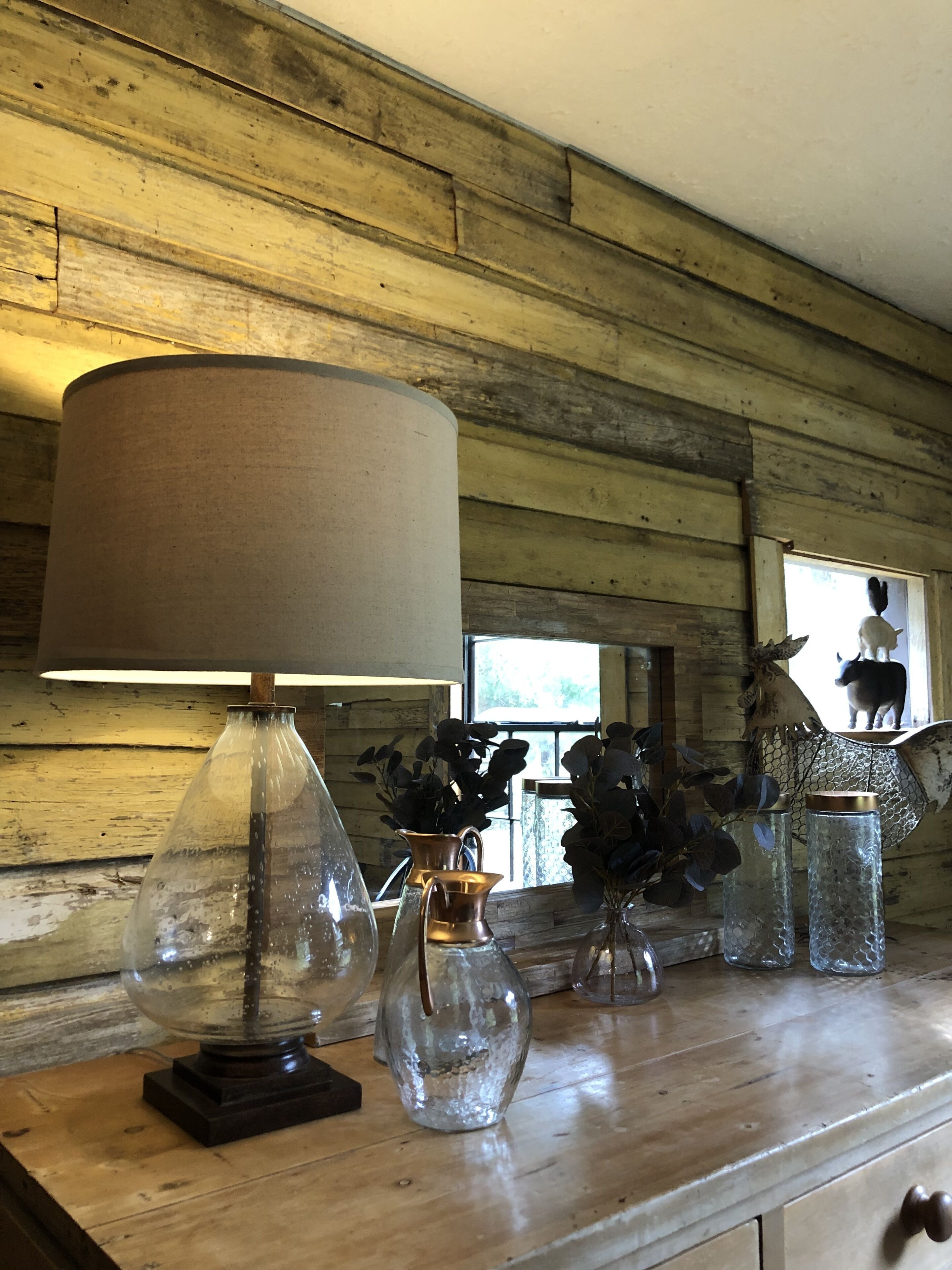 En trævæg med en rustik køkkenbordplade, der viser forskellige glasvaser og en lampe.