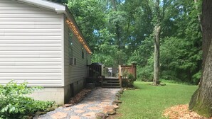 A pathway leading to a wooden deck with string lights, surrounded by a lush green garden and trees.