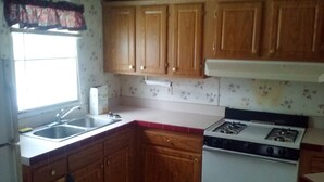 A kitchen with wooden cabinets, a gas stove, a sink, and a window with curtains.