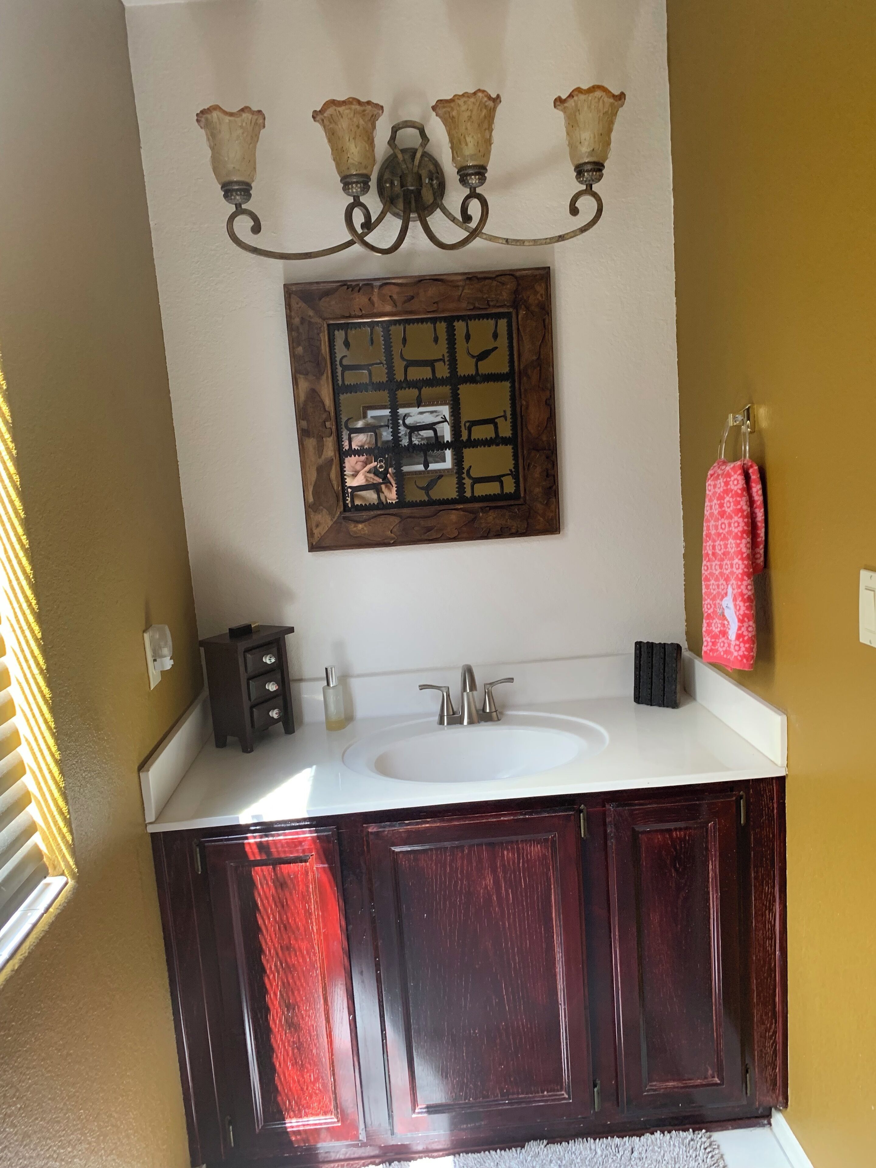 A bathroom with a white sink, dark wooden cabinets, a mirror with a decorative frame, and a chandelier with three lights.