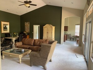 Una sala de estar con un sofá marrón, una mesa de centro de vidrio, un sillón estampado y un mueble de madera.