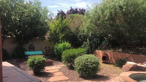 Un espace extérieur aménagé en patio, avec un sol en pierre, un banc vert et divers arbustes.