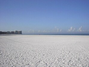 Une vaste plage dégagée, avec un ciel clair et des bâtiments visibles au loin.
