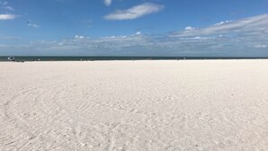 A wide, open sandy beach with a clear sky and calm sea.