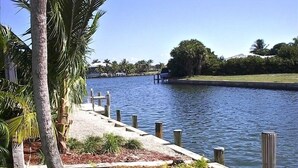 A waterfront walkway with a palm tree and a dock extending into a calm body of water.