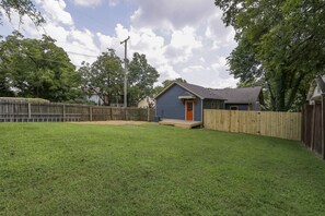 A backyard with a small house, a wooden fence, and a grassy lawn.