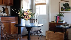 Une cuisine avec des meubles de rangement en bois, un réfrigérateur noir, une table à manger avec des chaises et un vase de fleurs.