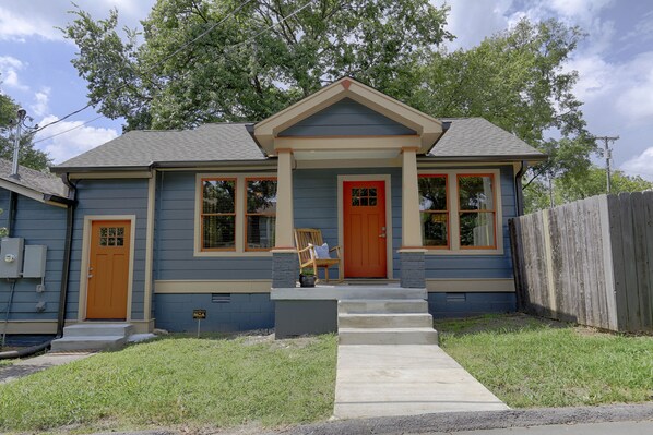 A two-story house with a front porch, a red door, and a small front yard.