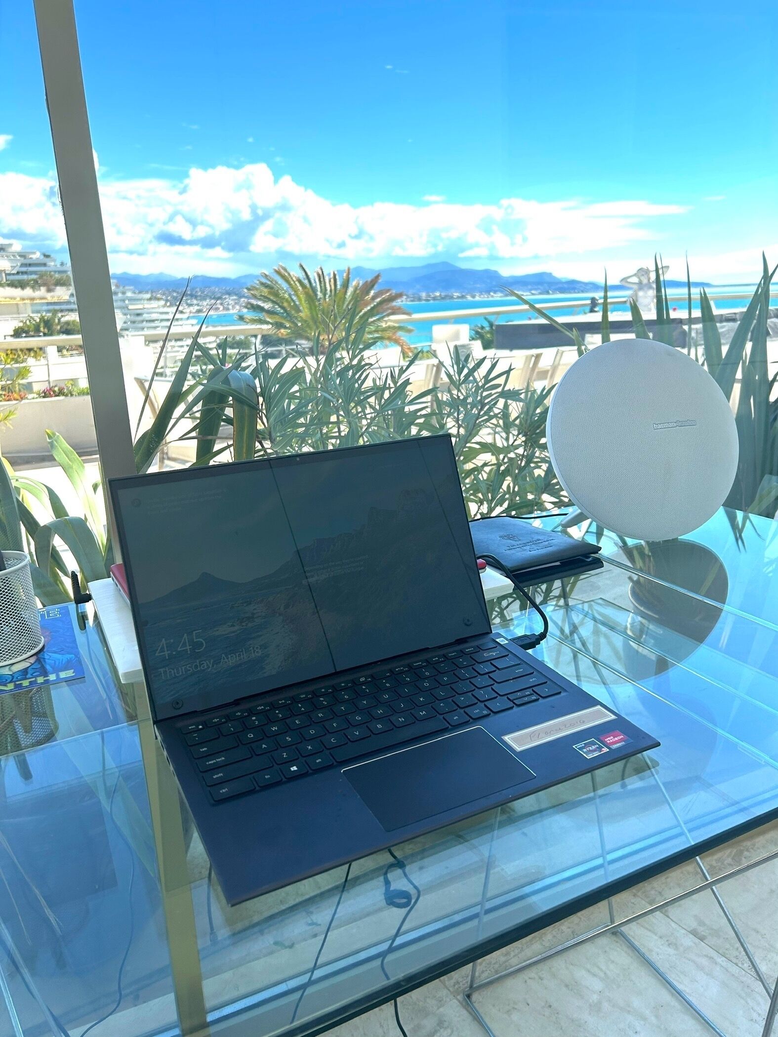 Ein Laptop auf einem Glastisch mit Blick auf Strand und Berge im Hintergrund.
