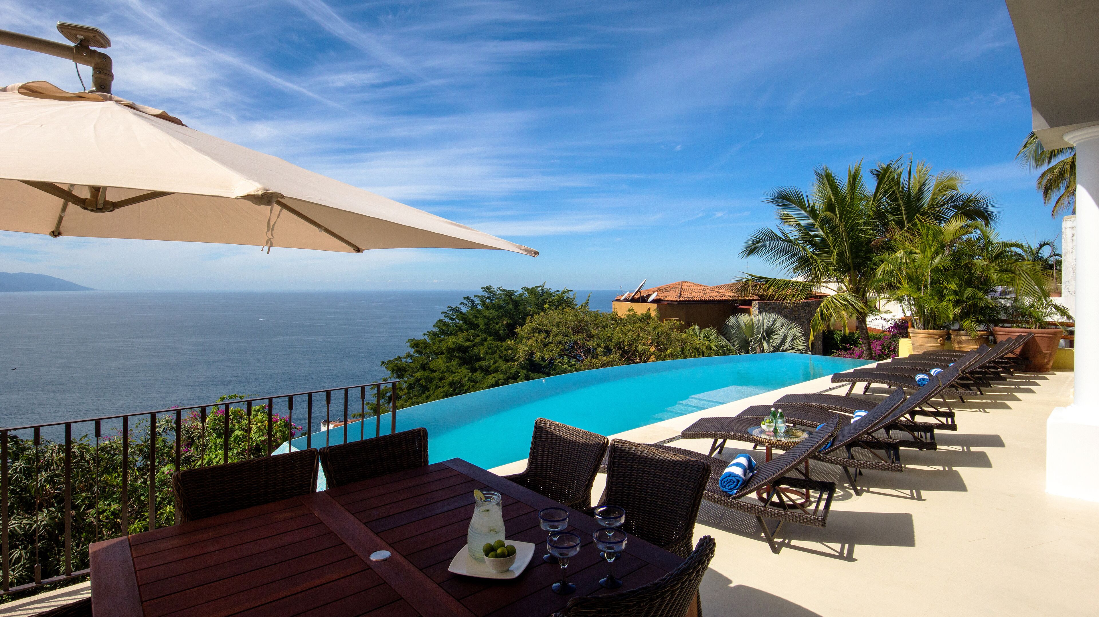 A poolside area with lounge chairs, a table with drinks, and a view of the sea.