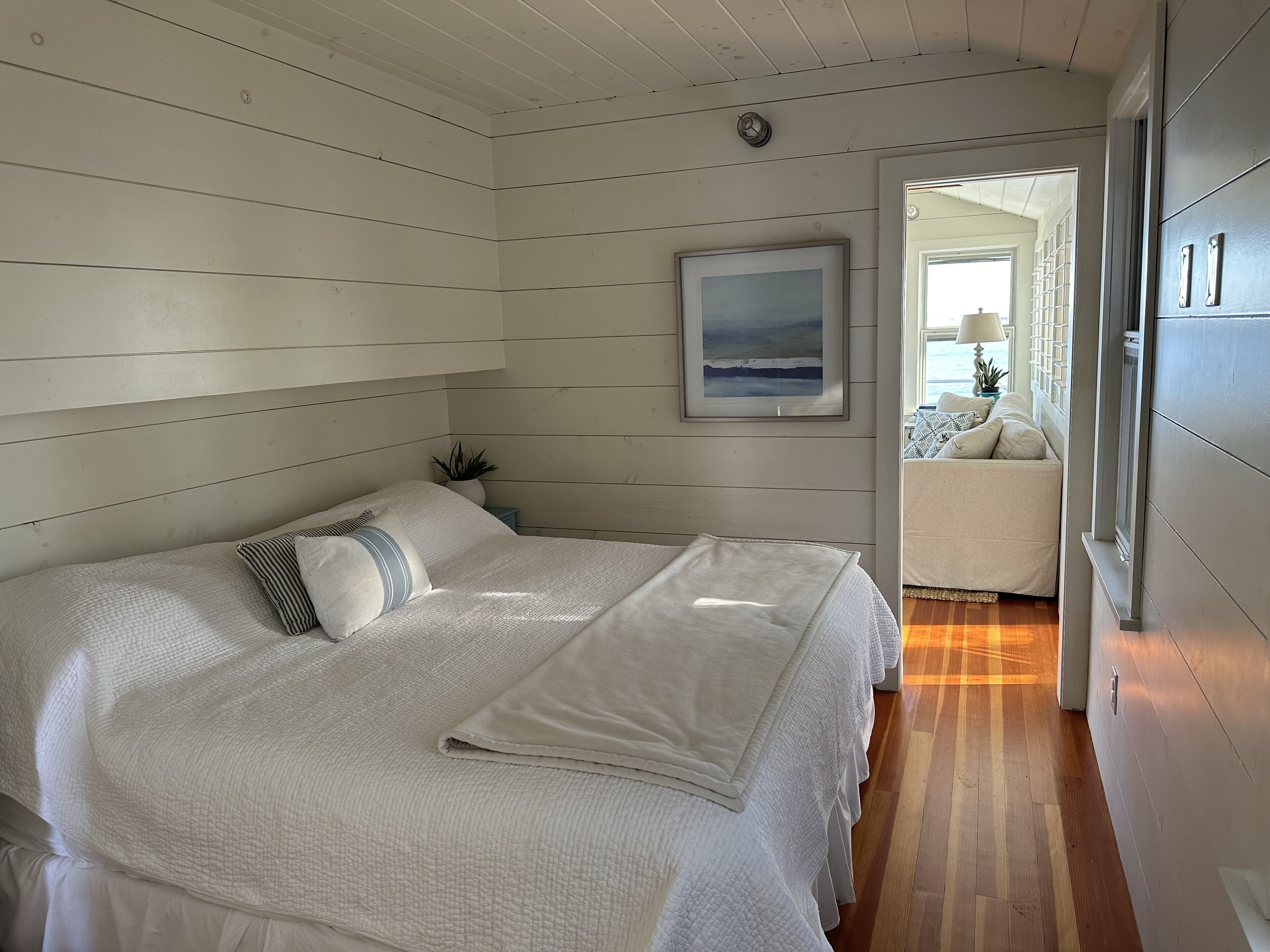 A bedroom with a large bed, a framed picture on the wall, and a view of a balcony through an open door.