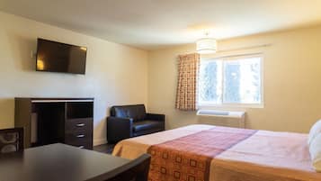 Quarto de hotel com cama, escrivaninha, cadeira, televisão e janela com cortinas.