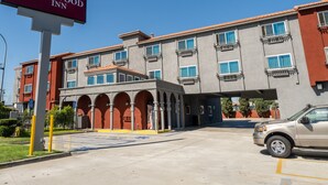 A Maywood Inn building with a red and gray facade, multiple balconies, and a parking lot. - Maywood Inn (Maywood)