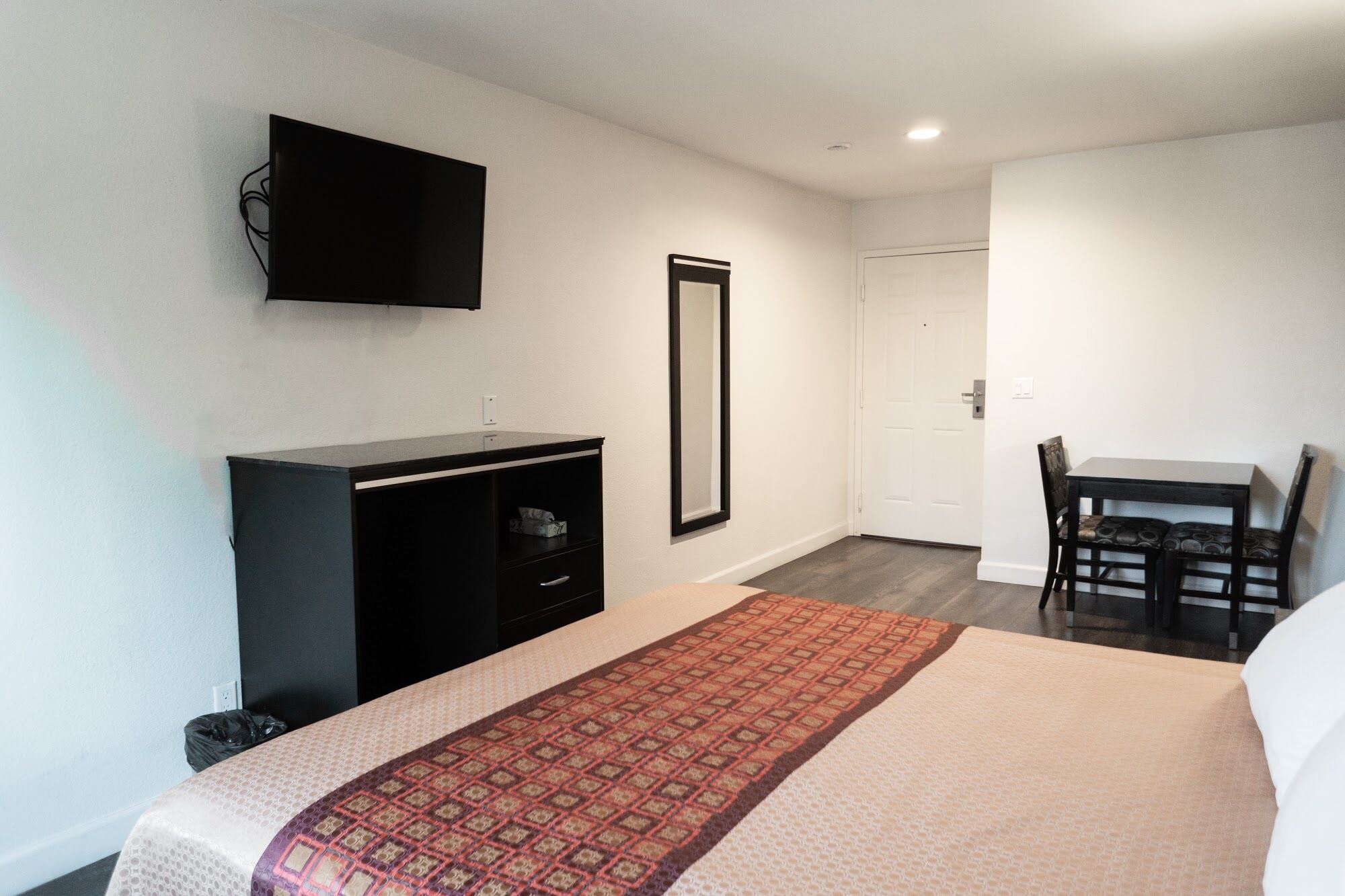 Habitación de hotel con cama, escritorio, silla, televisor montado en la pared y puerta que da a otra habitación.