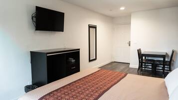 Habitación de hotel con cama, escritorio, silla, televisor montado en la pared y puerta que da a otra habitación.