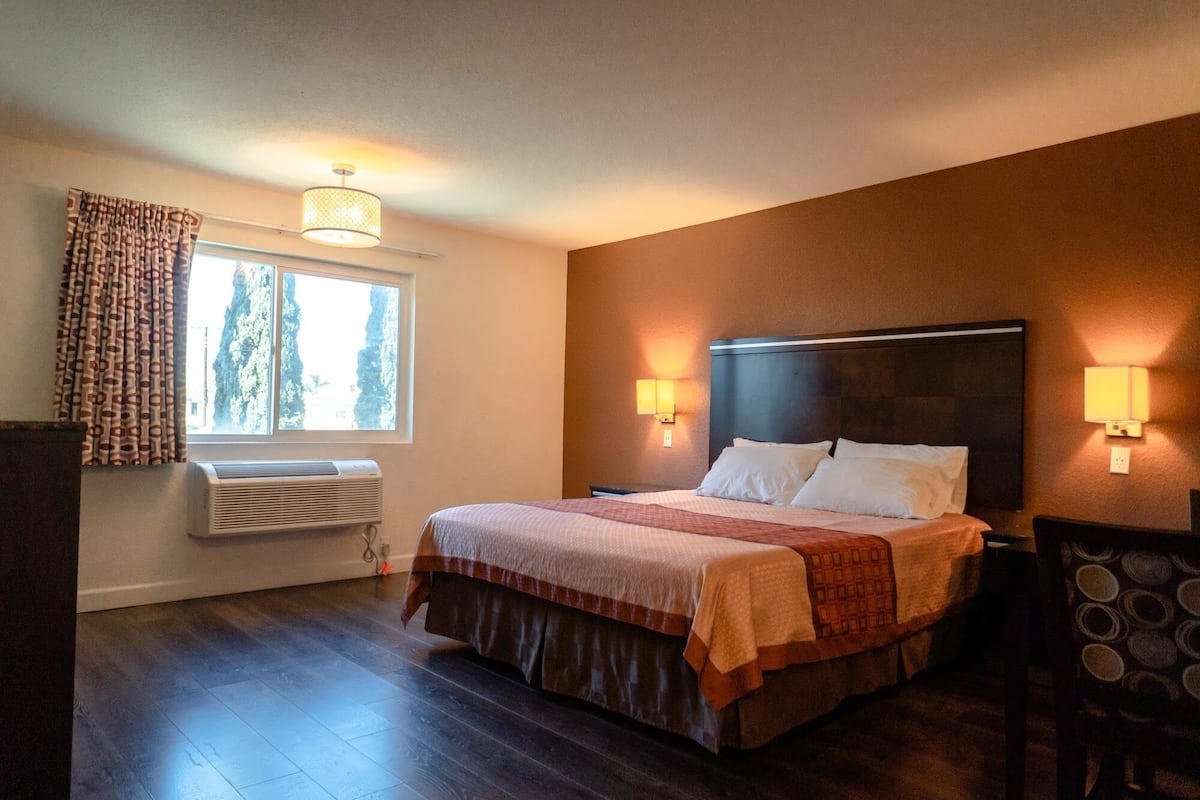 A hotel room with a large bed, two bedside lamps, a window with curtains, and a wall-mounted heater.