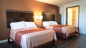 A hotel room with two beds, each with a patterned bedspread and white pillows. There are wall-mounted lights above the beds and a door leading to another room. - Maywood Inn (Maywood)