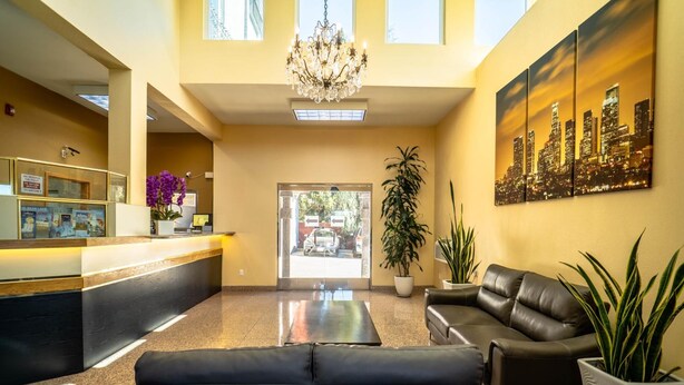 A hotel lobby with a reception desk, black leather sofas, a chandelier, and a cityscape painting. - Maywood Inn (Maywood)
