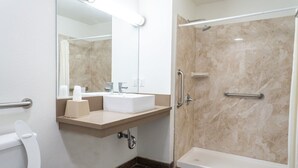 A modern bathroom with a white sink, mirror, and shower. - Maywood Inn (Maywood)