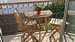 Ein Balkon mit Holztisch und Stühlen, einem Blumentopf und einem Metallgeländer.
