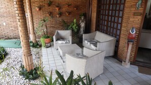 Een terras met rieten meubilair, plantenpotten en een bakstenen muur.