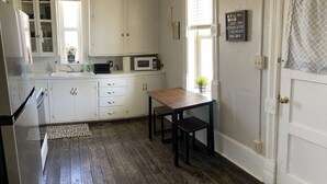 Een keuken met witte kastjes, een magnetron en een houten tafel.