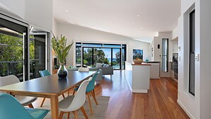A modern kitchen with a dining area, large windows, and a view of the outdoors.