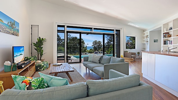 A modern living room with a large sliding glass door leading to a pool area, a flat-screen TV, and a bookshelf.
