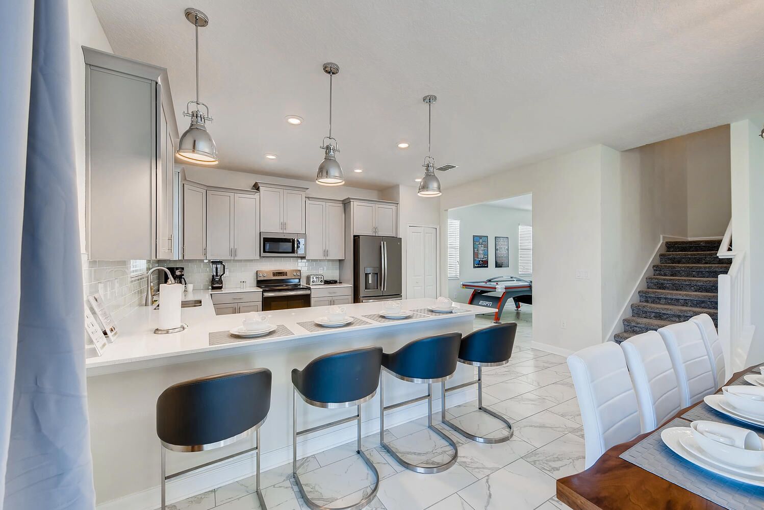 Una cocina moderna con una isla central, taburetes de bar y un comedor con mesa y sillas.
