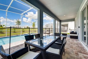Un porche techado con una mesa de vidrio y sillas de mimbre, con vistas a una piscina y un jardín.