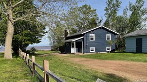 A two-story house with a garage, a fenced yard, and a view of the water. - Beautiful, private oceanfront cottage on the Bay of Fundy (Port Williams)