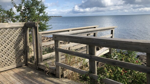 A wooden deck with a lattice fence, overlooking a calm body of water and a distant shoreline. - Beautiful, private oceanfront cottage on the Bay of Fundy (Port Williams)