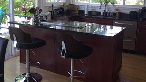 Een moderne keuken met een centraal eiland, twee barkrukken en grote ramen voor natuurlijk licht.