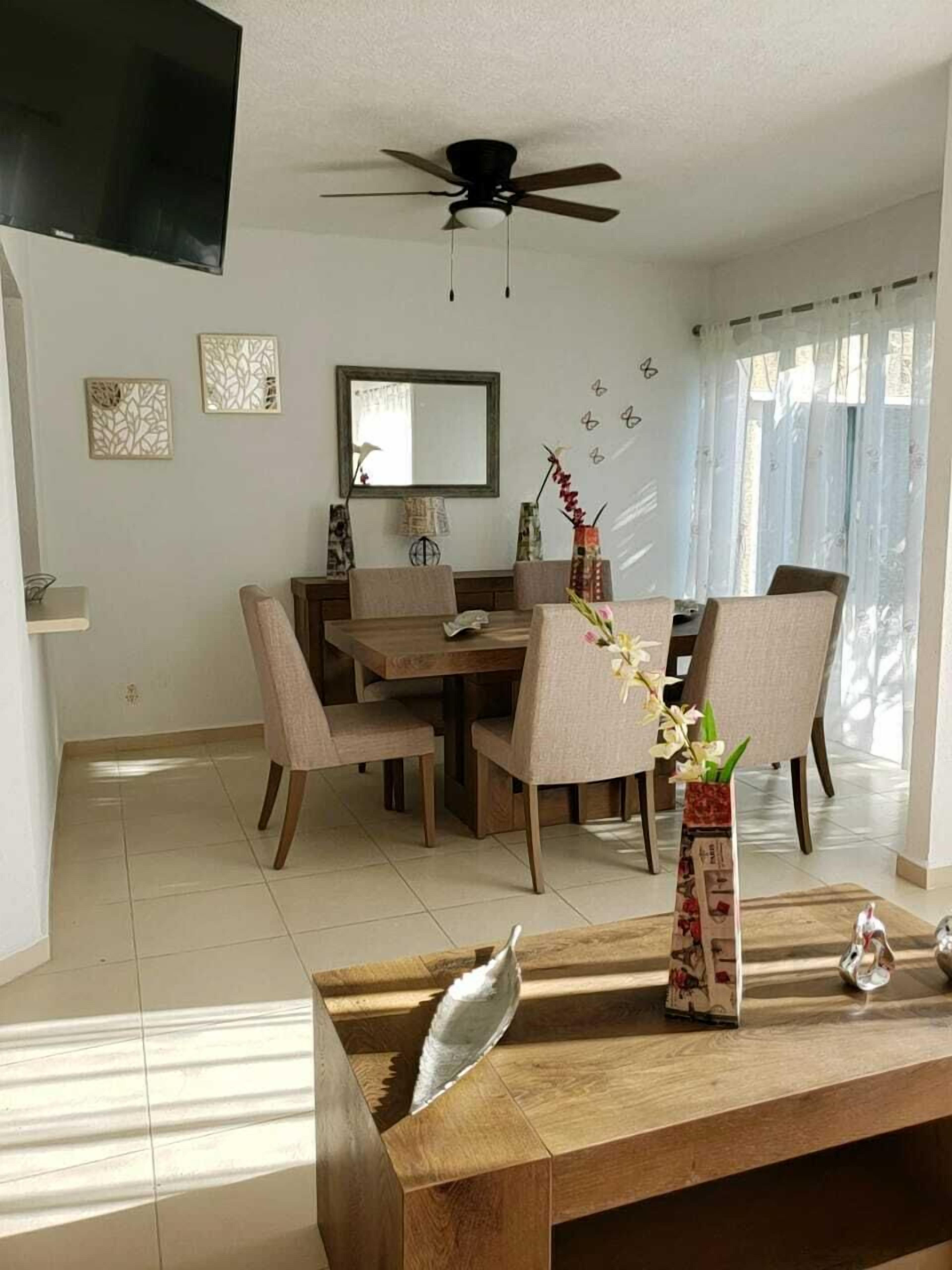 A dining area with a wooden table and chairs, a ceiling fan, and a large mirror on the wall.