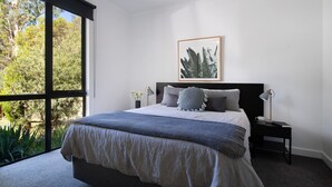 A bedroom with a large window, a bed with a gray and white duvet, two bedside lamps, and a framed picture on the wall. - Ablac House - Tranquil Bushland Getaway (Wheatsheaf)