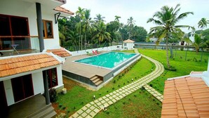 Ein Swimmingpool, umgeben von einem gepflegten Rasen und Palmen, mit einem Haus mit einem Ziegeldach und einem Balkon.