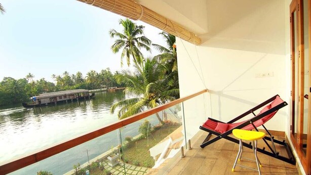 Ein Balkon mit Blick auf einen Fluss, Palmen, ein Boot und einen roten und gelben Stuhl.