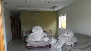 Ein Hotelzimmer mit zwei großen weißen Teddybären auf einem Bett, einem Fenster mit Jalousien und einem Flur zu weiteren Zimmern.