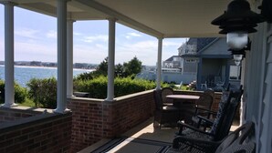 A covered patio with a view of the ocean, featuring wicker furniture and a brick wall. - HAMPTON BEACH OCEANFRONT HOME SITUATED ON GREAT BOARS HEAD (Hampton)
