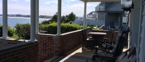 A covered patio with a view of the ocean, featuring wicker furniture and a brick wall.