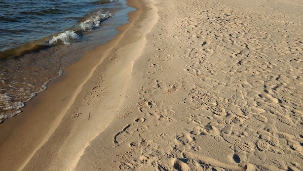 Una playa con huellas en la arena y un cielo despejado.