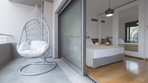 Un dormitori modern amb un llit gran, una cadira penjant i una porta corredissa de vidre que dona a un balcó.
