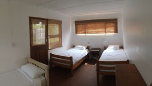 Una habitación pequeña y sencilla con dos camas de madera, una mesita y una ventana con persianas de bambú.