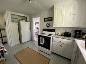 A compact kitchen with white cabinets, a stove, a refrigerator, and a coffee maker.