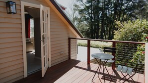 Una terraza de madera con una mesa y sillas, barandal rojo y una puerta que da a un cuarto interior.