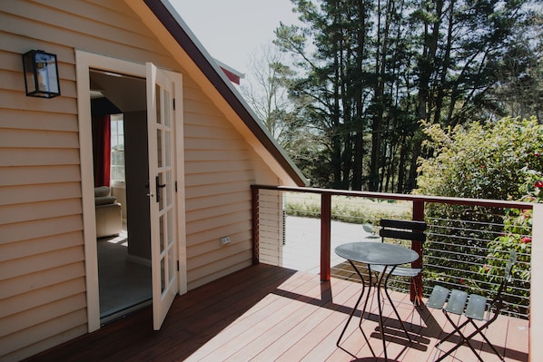 A wooden deck with a table and chairs, a red railing, and a door leading to an interior room.